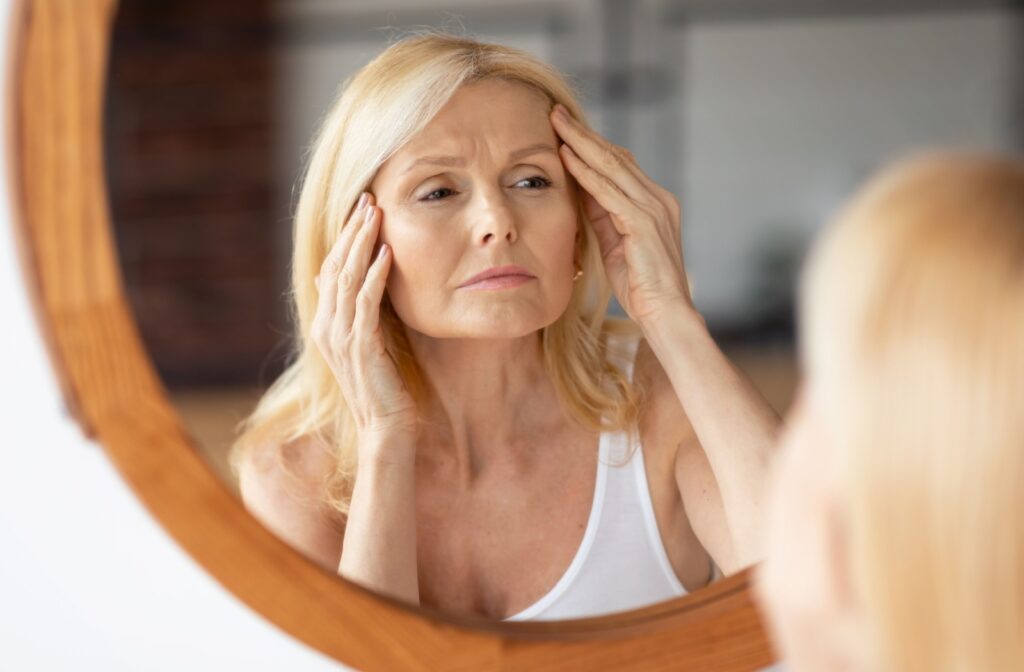 Middle-aged woman looking in the mirror touching her face & examining her frown lines.
