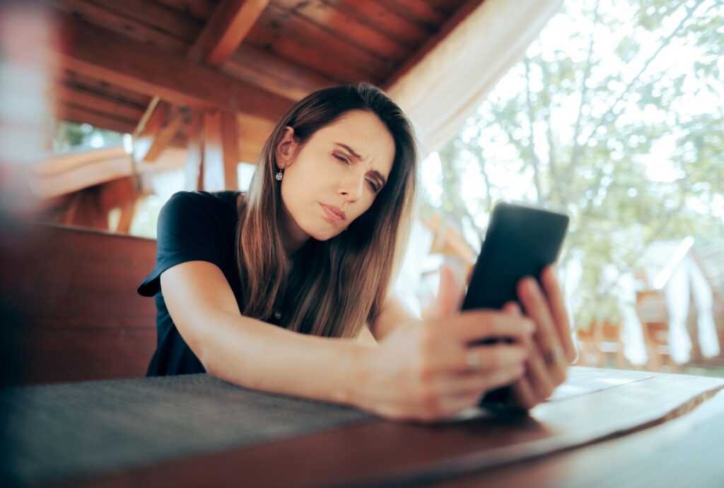 A young woman squinting to try and read her phone with blurry vision from dry eyes.