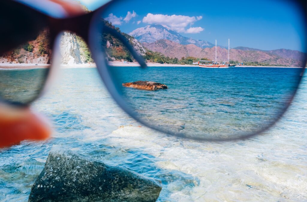 A hand holds their polarized sunglasses against calm waters to see if they enhance color contrast, reduce light glare, and improve visual clarity.